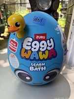 Front view of blue egg-shaped toy packaging featuring the yellow duck head and "Eggy Wawa Learn in the Bath" branding