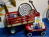 Photo showing large red Berlin Express wooden wagon and small red Radio Flyer wagon filled with toys, dartboard resting in larger wagon