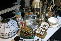 Table display showing assortment of lamps, candle holders, jars, and decorative ceramics.