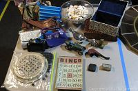Photo showing assorted purses, metal and tin trinkets, ceramic solitaire marbles game, glass bingo card plate, blue velvet lined box, and bowl with beach shells.