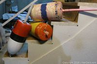 Three authentic Maine buoys placed on stair steps, showing color and condition with chipped paint on poles and bodies.