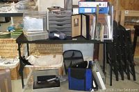 Photo of a desk with binders, mesh organization trays, books, presentation stand, and some stacked folded chairs.