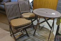 Wooden brown round bistro table with two matching wooden folding chairs each with brown polka dot cushions tied on seat