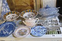 Front view of assorted serving plates, bowls, teapot, and lidded tureen on shelf