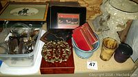 Wide view of lot contents showing faux stone planters, multiple framed art pieces, small red dictionaries stacked in blue bucket, brass trivets, ceramic cups, and small frame stands
