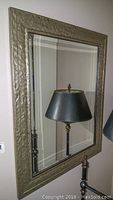 Full view of the wall mirror showing its textured metallic frame and clear glass surface.