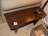 Wooden bench/end table showing the wood texture and brown finish with items on top including a lamp and reed diffuser