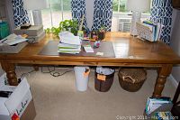 Full view of the pine wood farmhouse table in a room setting with items on top and baskets and bins beneath, showing table legs and surface.