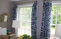 Two blue and white drapes with a geometric pattern hanging on curtain rods with rings in front of two windows.