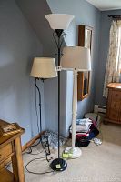 Three floor lamps of different styles and heights standing side by side in a room corner near a window and wooden furniture.