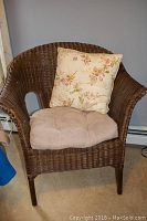 Dark brown wicker chair with beige seat cushion and floral back cushion against a gray wall and white baseboard heater.