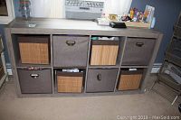 Front view of wooden storage unit with 8 cubby storage bins, four bamboo-style and four fabric bins.