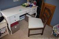 White wooden desk with multiple drawers and curved legs alongside a wooden ladder back chair with cushioned seat on wheels in a room setting.