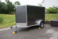 Three‐quarter front view showing overall enclosed trailer, aluminum diamond plate front guard, ball coupler hitch and scissor jack