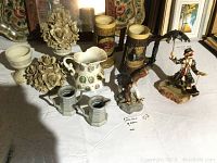 Photo showing assortment of decorative ceramic jars with floral tops, various decorative steins, small pitcher, and painted clown figurine mounted on stone slab.