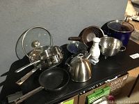 Overview of kitchen items on black surface showing stainless steel pans, kettle, colander, chopper, and crockpot
