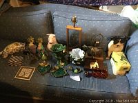 Wide view of all garden and animal themed home decor items arranged on a sofa for display, showing variety of items including lamps, door stops, ceramic dishes, small boxes, and animal figures.