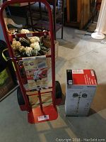 Milwaukee red hand truck with tags next to boxed UtiliTech work lamp in basement room setting.