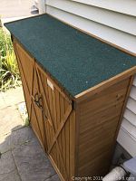 Exterior front view of wooden outdoor storage shed with double doors and green shingled roof