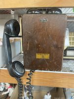 Front view of antique wooden telephone with handset attached and rotary dial on top.