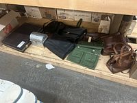 Shelf with all items: large brown briefcase, silver metal lunchbox, black canvas bag, green canvas bag, two brown handbags