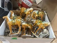Six ceramic horse figurines in a cardboard box, showing various poses and colors (brown body with green and white accents).