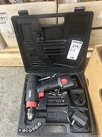 Open black plastic case containing cordless drill, battery charger, battery, and bits.