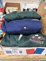 Box of folded Disney varsity jackets including navy and green colors with Mickey Mouse graphics and snap buttons.
