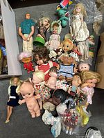 Wide view of the lot showing various dolls and toys including Big Boy doll, Kewpie dolls, blonde dolls, and others in mixed condition on floor.