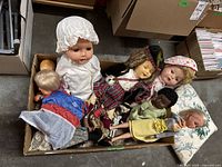 Wide shot of the box containing multiple dolls including porcelain and plastic dolls in various outfits.