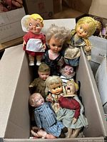 Box of 9 vintage dolls made of composite and similar materials, showing wear and damage.