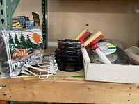 Camper cover blanket in packaging with camping graphics, E-Z Cord wrap reels, white metal wall hooks, squeegees on a wooden shelf.