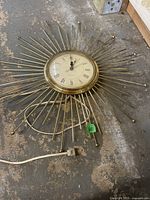 Full view of Mid-century Modern Deco starburst wall clock showing brass metal design and power cord