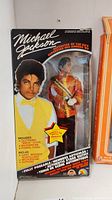 Front view of the Michael Jackson doll in original packaging showing the doll dressed in red and gold stage outfit and the packaging with image of Michael Jackson.