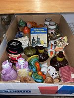 Top view photo of box containing multiple novelty salt and pepper shakers of animal and travel souvenir themes, showing a variety of colors and shapes.