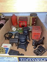 Box containing vintage kitchen and bath tins, novelty pencil sharpener, black cast iron stove figures, and a cast iron dog figurine