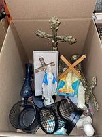 Overview of lot in cardboard box showing brass crucifix, blue vase, desk organizers, wooden crosses and statues