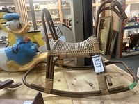 Side view of the rattan rocking horse, showing woven seat and curved wooden rockers with visible wear and cracks.