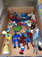 Box of various action figures including superheroes and Smurfs seen from front angle