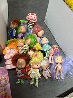 Multiple vintage dolls including Strawberry Shortcake figures and assorted small dolls with varying hair colors and clothing conditions.