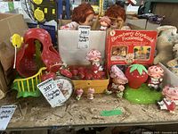 Wide view of Strawberry Shortcake toys, figures, game basket, clock, and red playground structure on table
