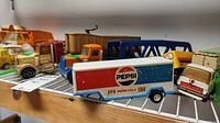 Assortment of vintage toy trucks and trailers including Pepsi-Cola trailer, Kenworth Tow Truck, and various other trucks on a metal rack.