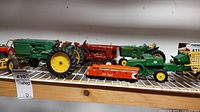 Photo showing a lineup of toy tractors and a CP Rail train on a white metal shelf, details visible include color and condition of each toy.