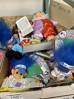 Box containing various troll dolls including Toronto Blue Jays themed trolls with bright blue hair and some dolls in original packaging.