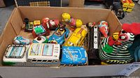 Full view of the collection of colorful vintage metal wind-up toys in a cardboard box showing animals, buses, cars, and a train engine.