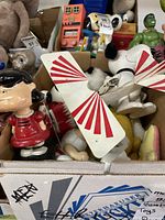 Lot featuring various Peanuts toys including Snoopy metal airplane, Lucy bobblehead, Woodstock plush, and other character collectibles.