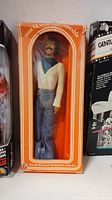 Front view of the vintage Sonny Bono doll in original orange packaging with clear window showing the doll wearing a white and black top and blue jeans.