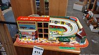 Full top and side view of the vintage tin lift garage toy featuring the service station and race track with colorful printed details and 3D elements.
