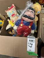 Box containing vintage toys including the Mario figure wrapped in plastic, a detailed building or house toy, and other assorted toys.