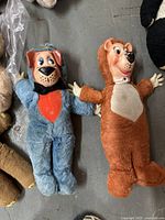 Full view of blue dog and brown teddy bear plush toys with rubber faces lying on floor.